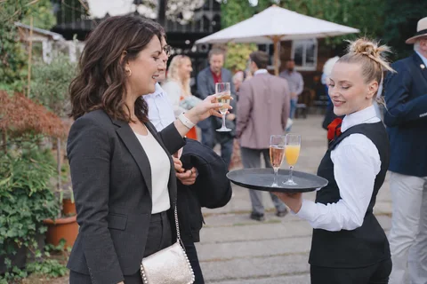 A show waitress serves a drink from a tray to a wedding guest.