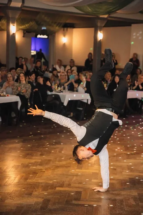 A show waiter balances on one hand in front of the guests.