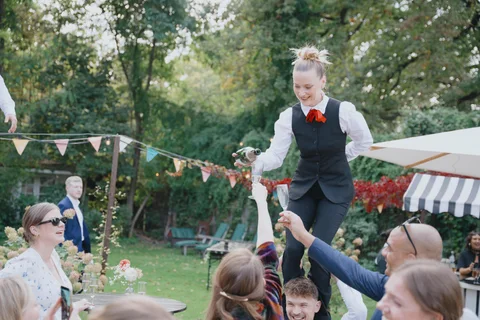 A show waitress pours drinks for guests while standing on her colleague’s shoulders.