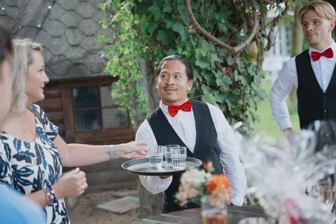 A show waiter holding a tray of glasses interacts with a wedding guest.