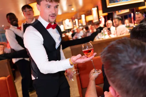 A show waiter balances a wine glass in front of guests.