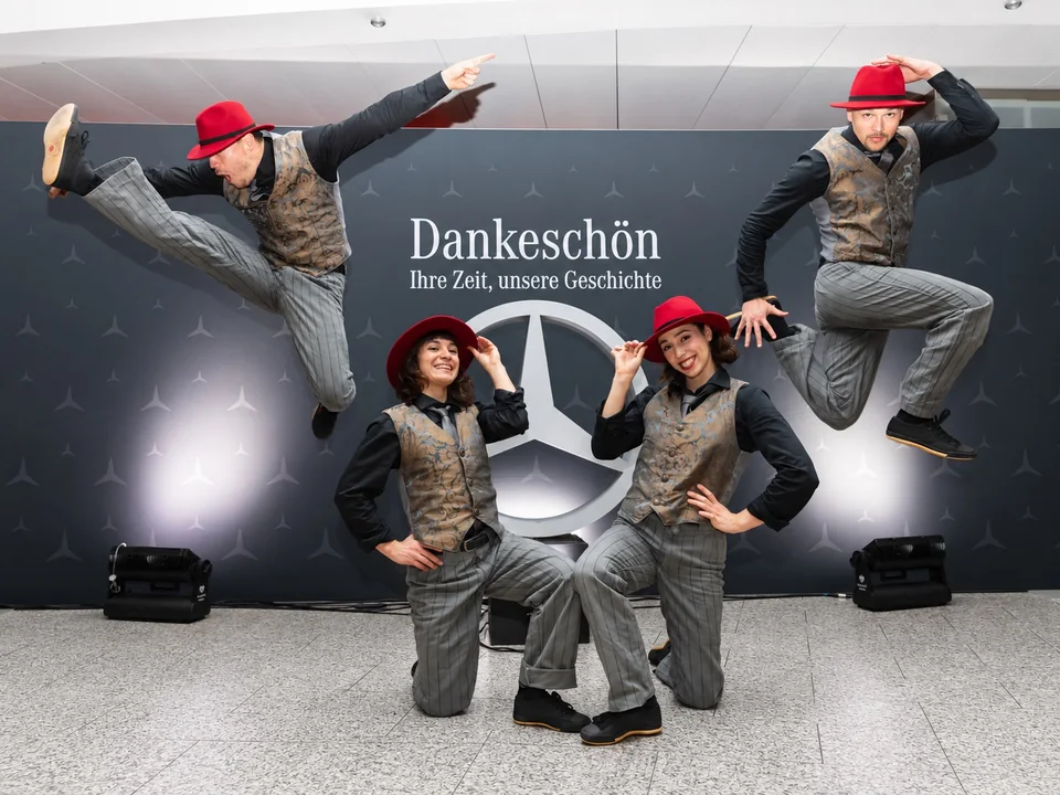 Four performers from The Funky Monkeys wearing red hats in front of a Mercedes-Benz photo backdrop.